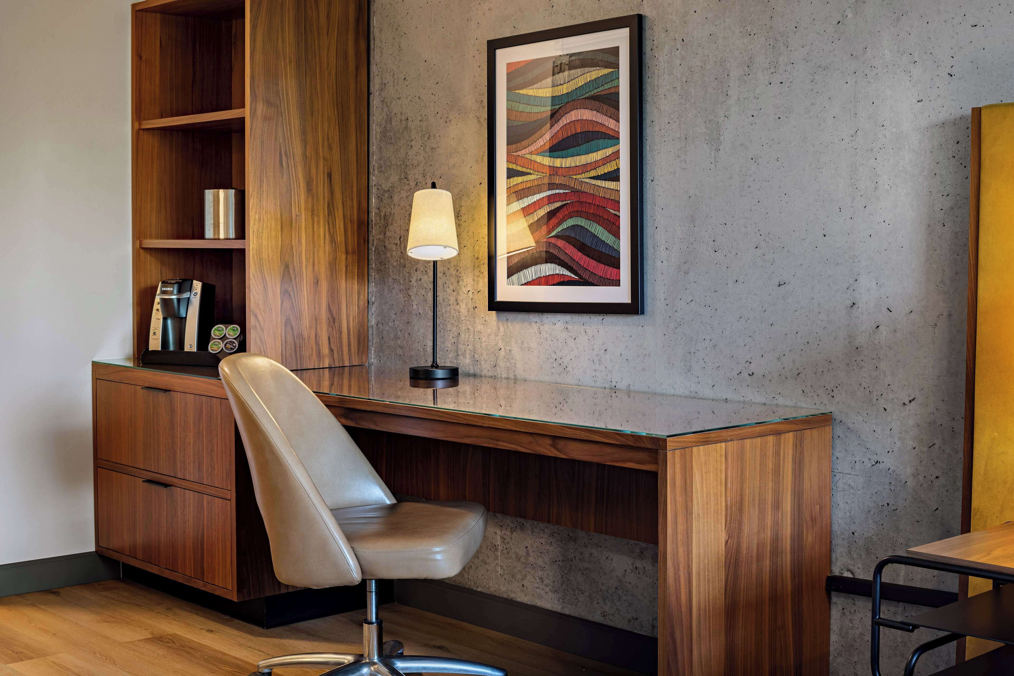 Un espace de bureau moderne avec un bureau en bois, un fauteuil en cuir, un tableau abstrait encadré et une lampe sur pied.