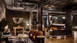 A modern lounge area with a wooden table, sofas, and potted plants. - The Loom Hotel, Tapestry Collection by Hilton (Warwick)