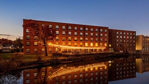 A large brick building with multiple windows and a reflection in the water. - The Loom Hotel, Tapestry Collection by Hilton (Warwick)