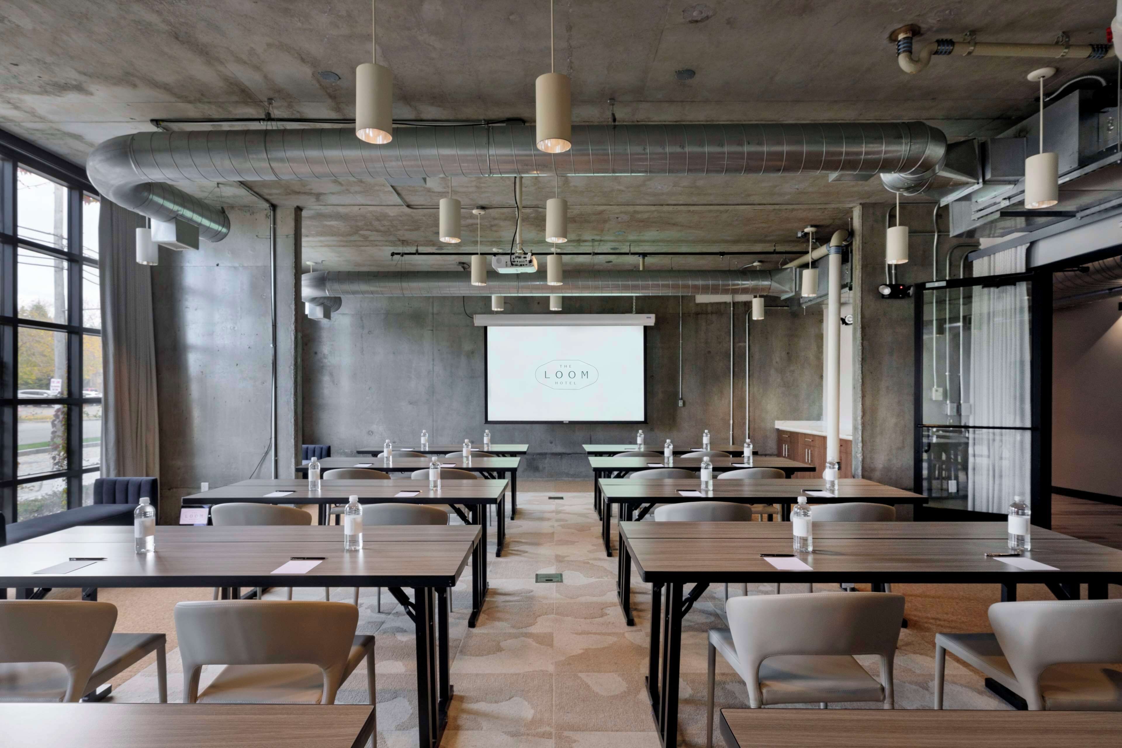 A conference room with tables, chairs, a projector screen, and a large window.