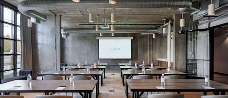 A conference room with tables, chairs, a projector screen, and a large window.