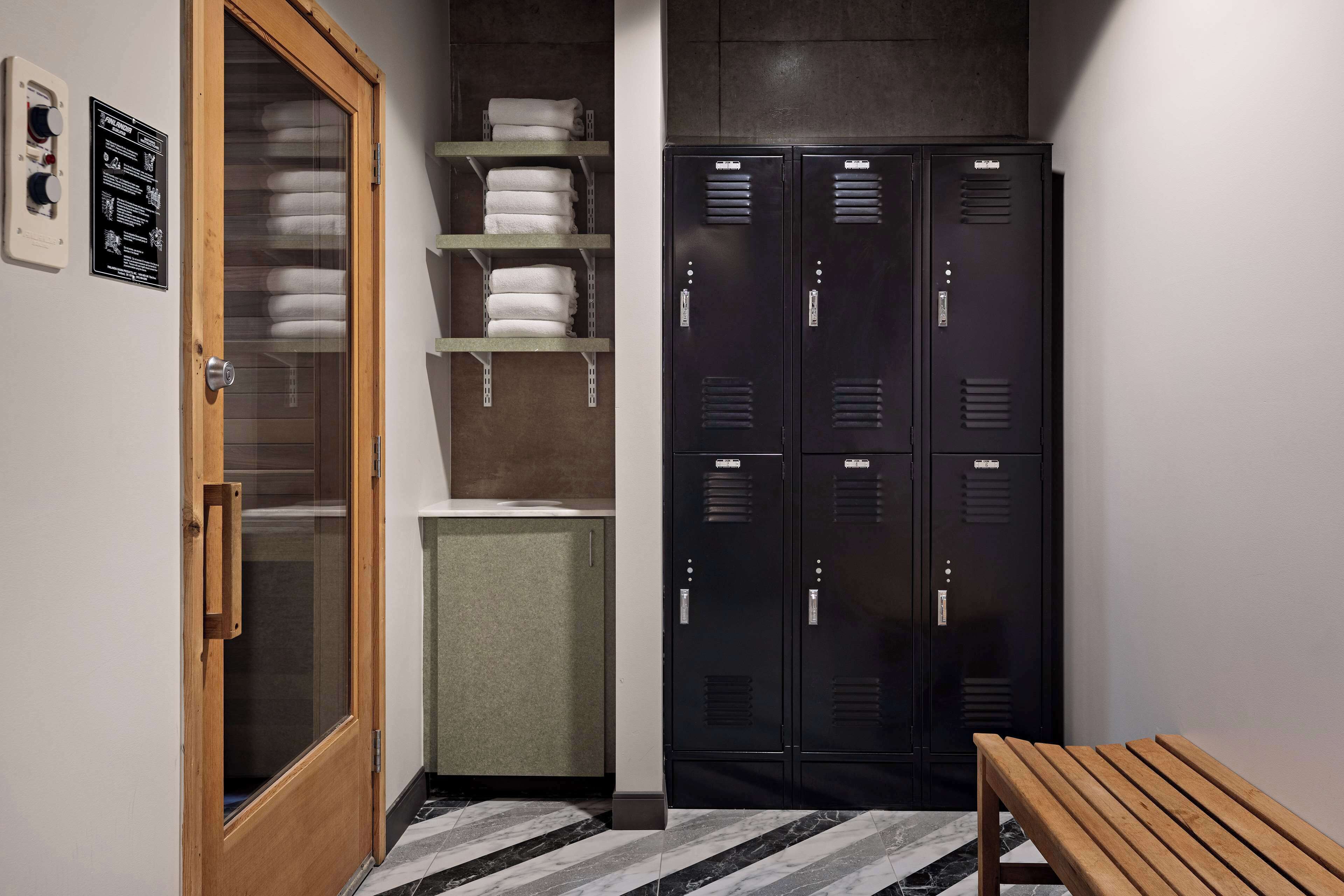 A hallway with a wooden door, a bench, and black lockers.