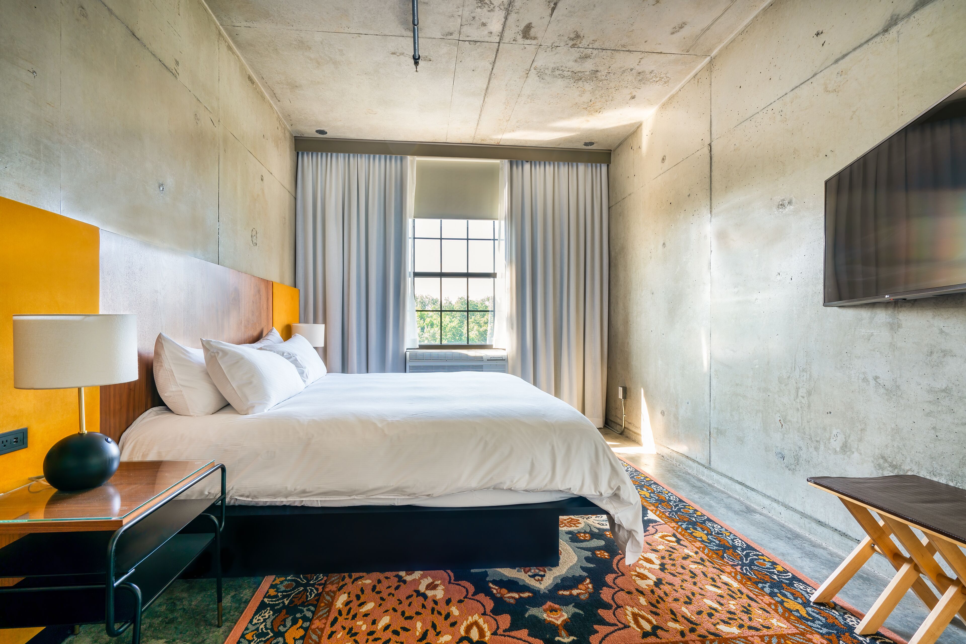 Una camera d'albergo moderna con un letto grande, una scrivania, una sedia, una televisione e una finestra con tende.