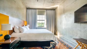A modern hotel room with a large bed, a desk, a chair, a TV, and a window with curtains.