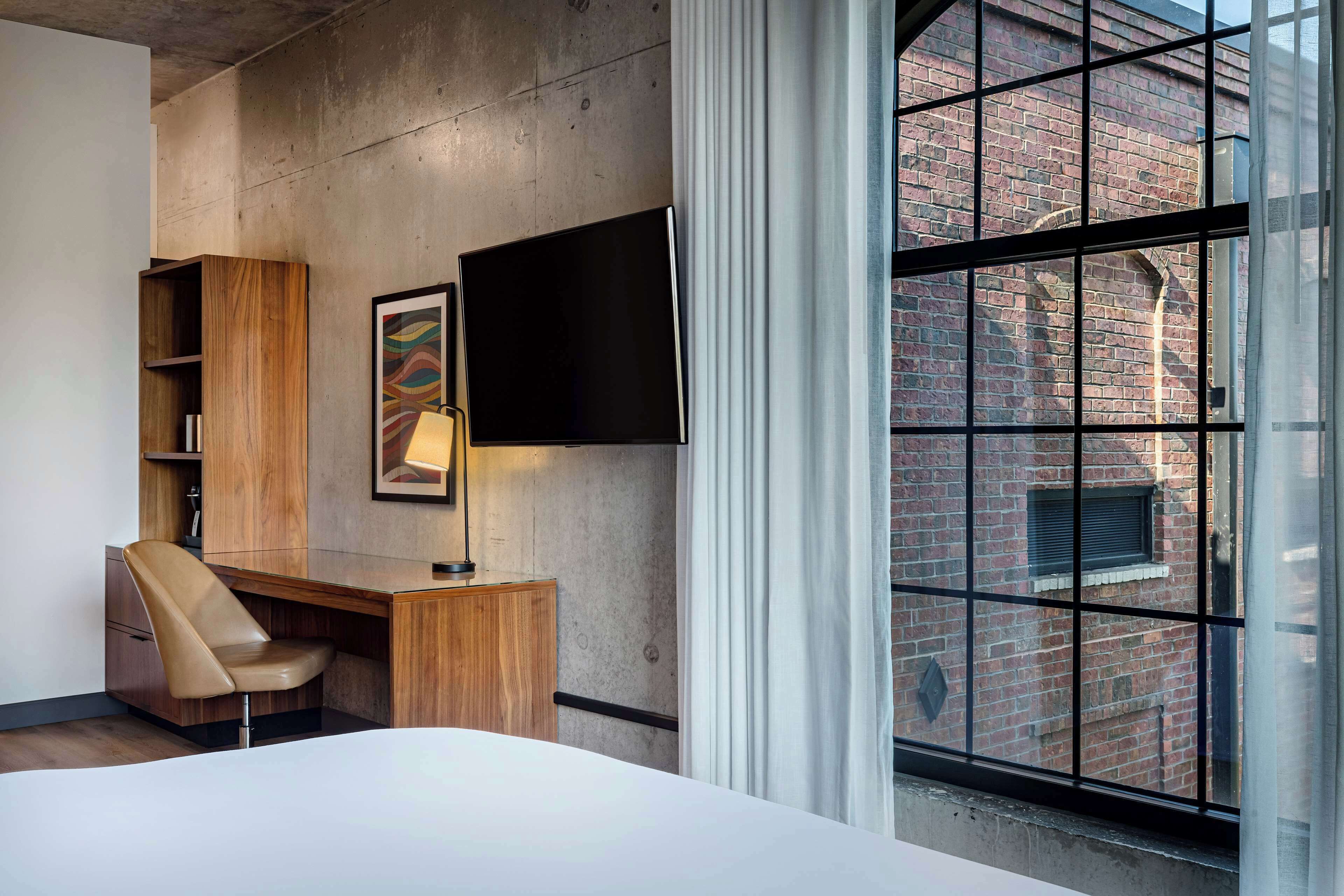 Una habitación de hotel moderna con un ventanal grande, un escritorio con silla, televisión de pantalla plana y una cama.