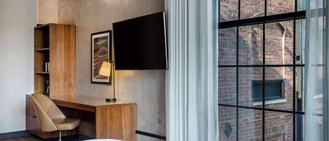 A modern hotel room with a large window, a desk with a chair, a flat-screen TV, and a bed.