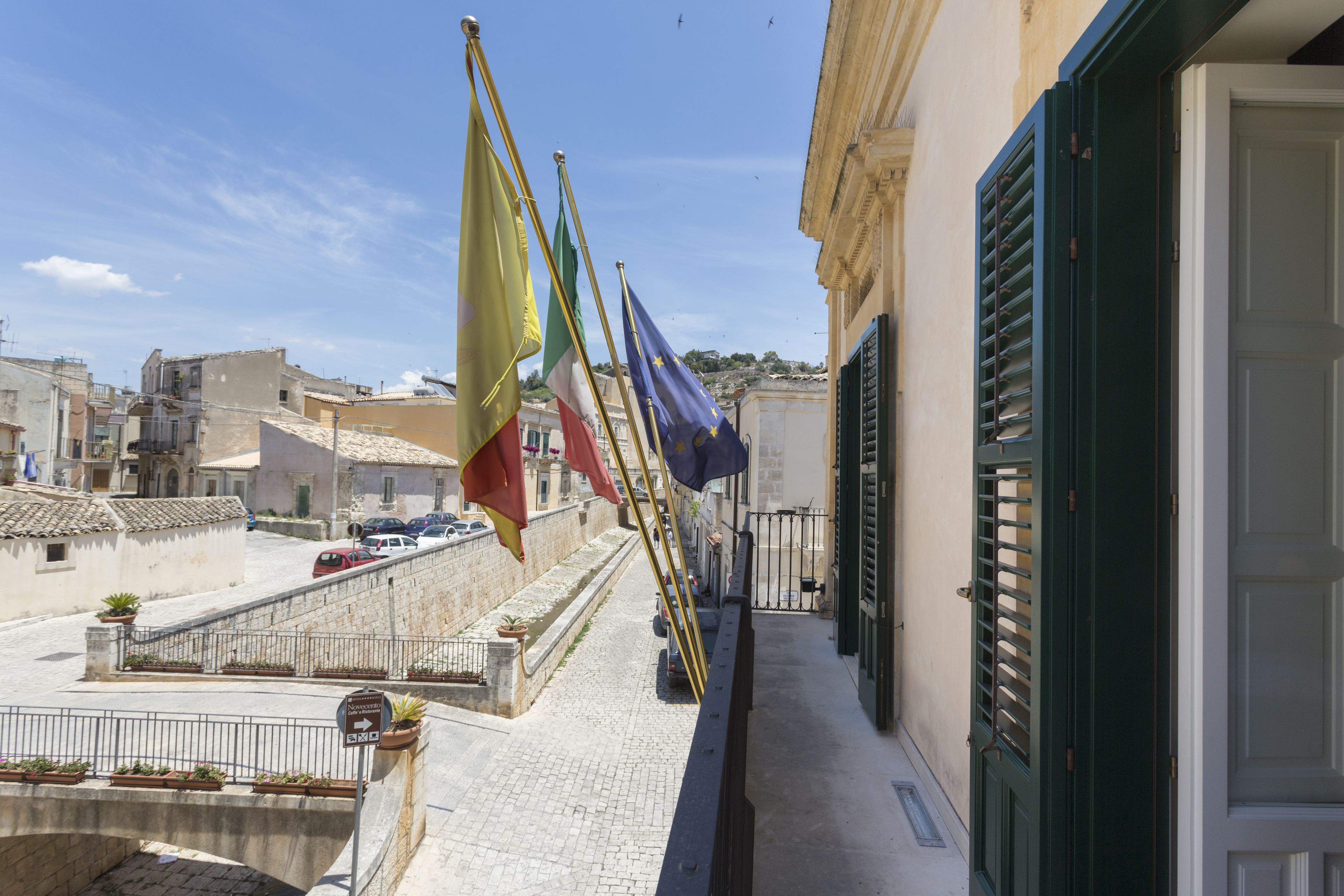 A balcony with flags, a stone wall, and buildings in the background.