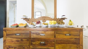 Un aparador de madera con varios cajones y un espejo encima. Sobre el aparador, hay varios cuencos con frutas diversas como sandía, manzanas, peras y plátanos.