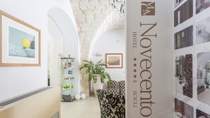 Un pasillo de hotel con una recepción, obras de arte enmarcadas, una planta en maceta y un sofá.
