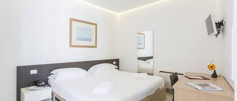 Una habitación de hotel moderna con una cama bien hecha, una mesita de noche con teléfono, un escritorio con silla y un televisor montado en la pared.
