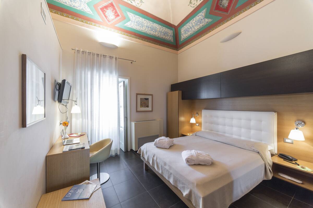 A hotel room with a bed, desk, chair, and a bathroom with a shower curtain.