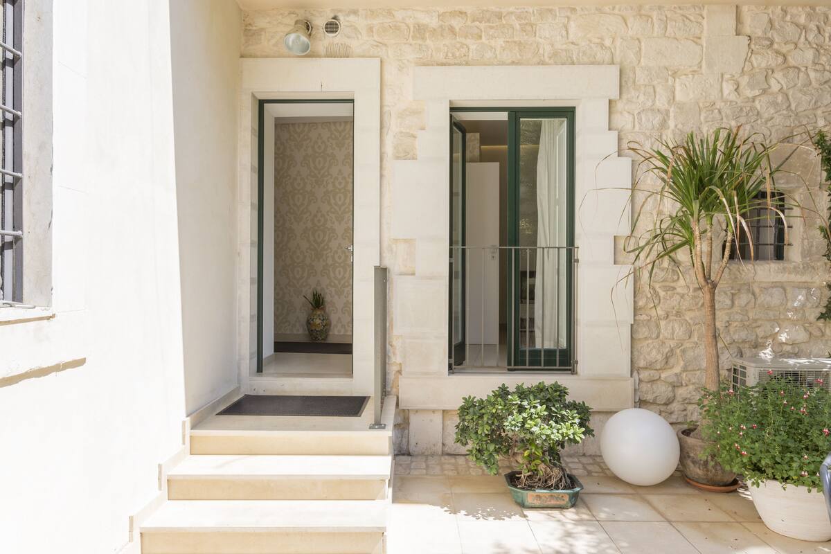 A stone building with a staircase leading to a door, potted plants, and a large white spherical object on the ground.