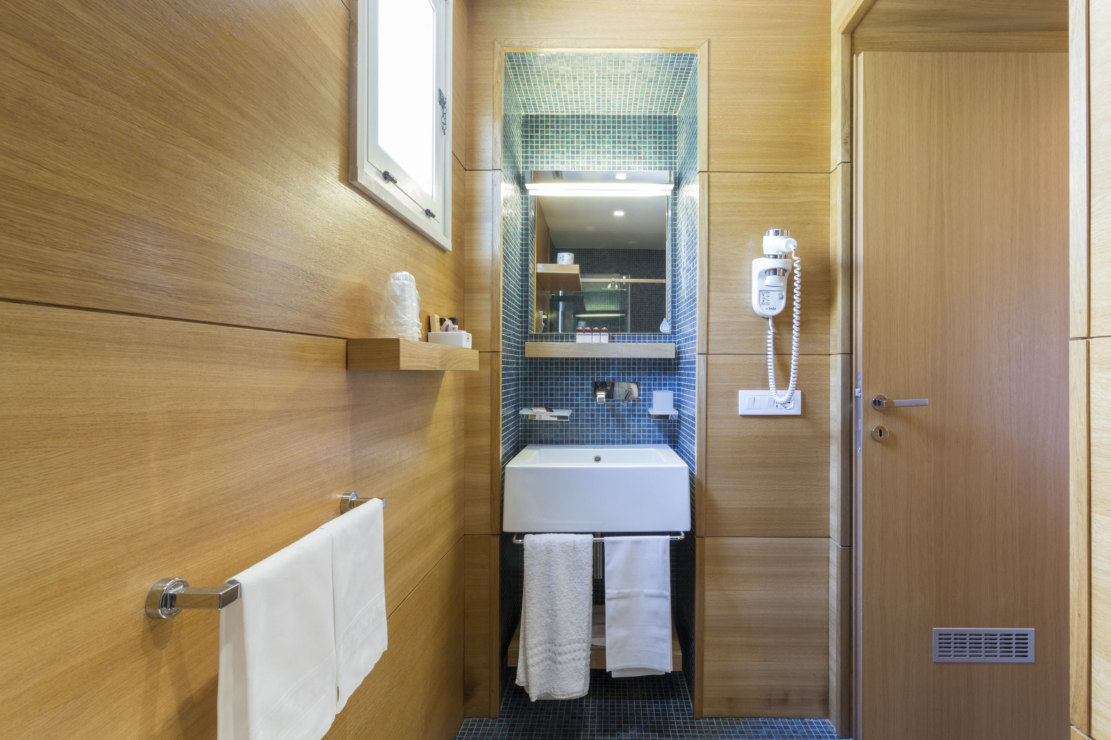 A bathroom with wooden walls, a white sink, a mirror with a blue-tiled backsplash, and a towel rack.