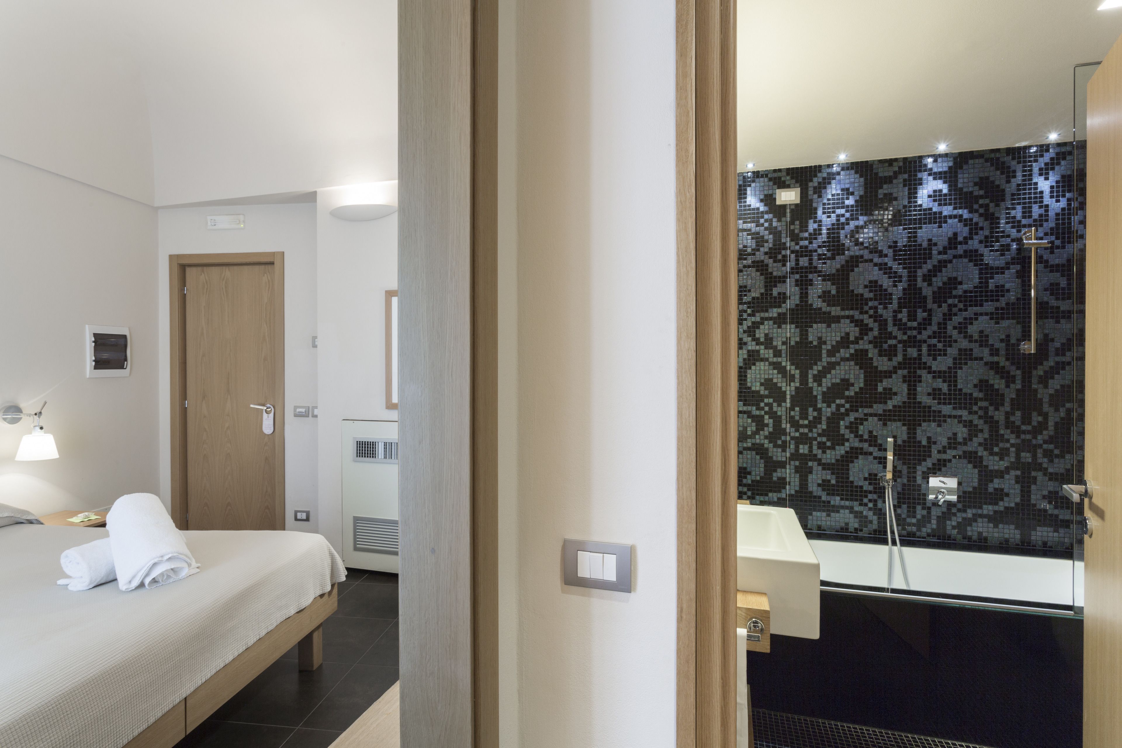 A hotel room with a bed, bedside table, and a bathroom with a shower and a mirror.