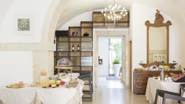 Un comedor con mesas dispuestas para una comida, una escalera que sube a un nivel superior y un espejo grande en la pared.