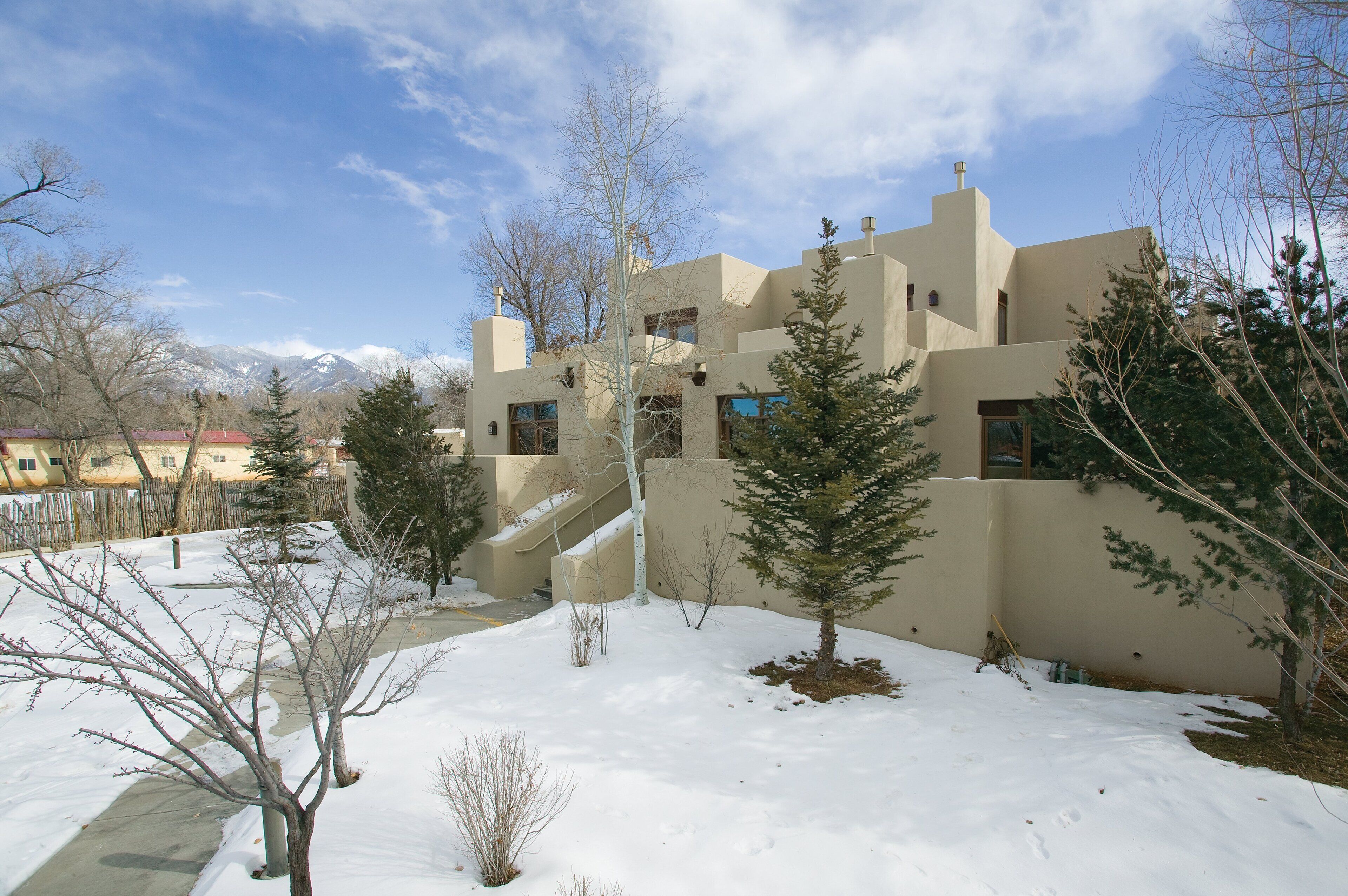 Une maison moderne avec une cour enneigée et des montagnes en arrière-plan.