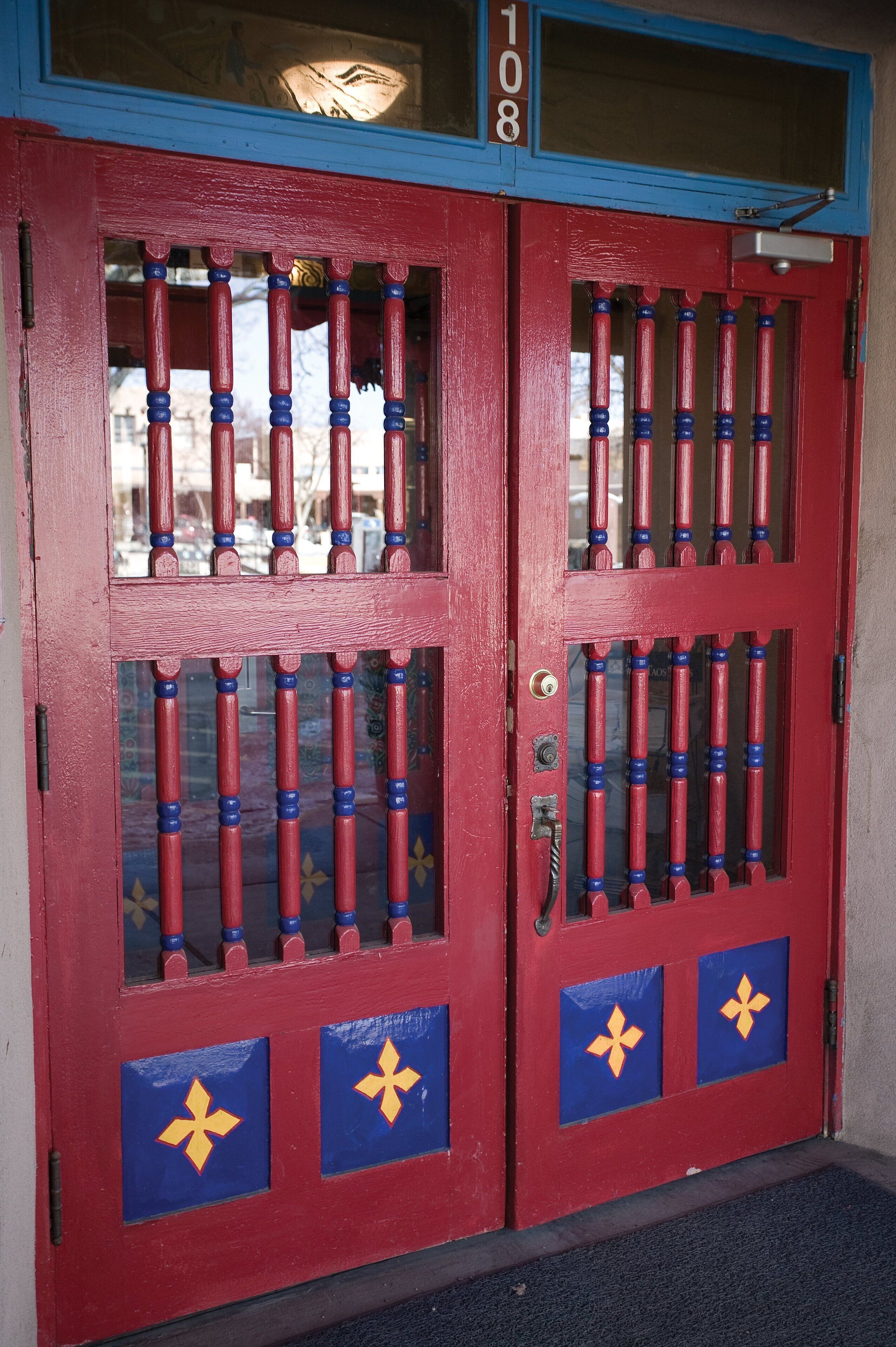 Una porta rossa con decorazioni blu e gialle, il numero '108' sopra e una maniglia metallica.
