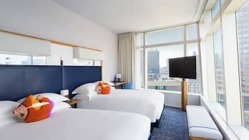A hotel room with two beds, a large window with a view of the city, a flat-screen TV, and a bench by the window.