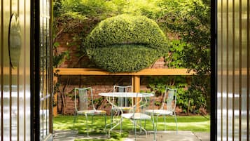 Un patio con mesa y sillas, rodeado de vegetación y un muro de ladrillo.