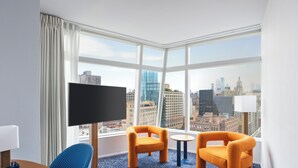 A hotel room with a large window, two orange chairs, a small round table, and a flat-screen TV. - The Standard East Village (New York)