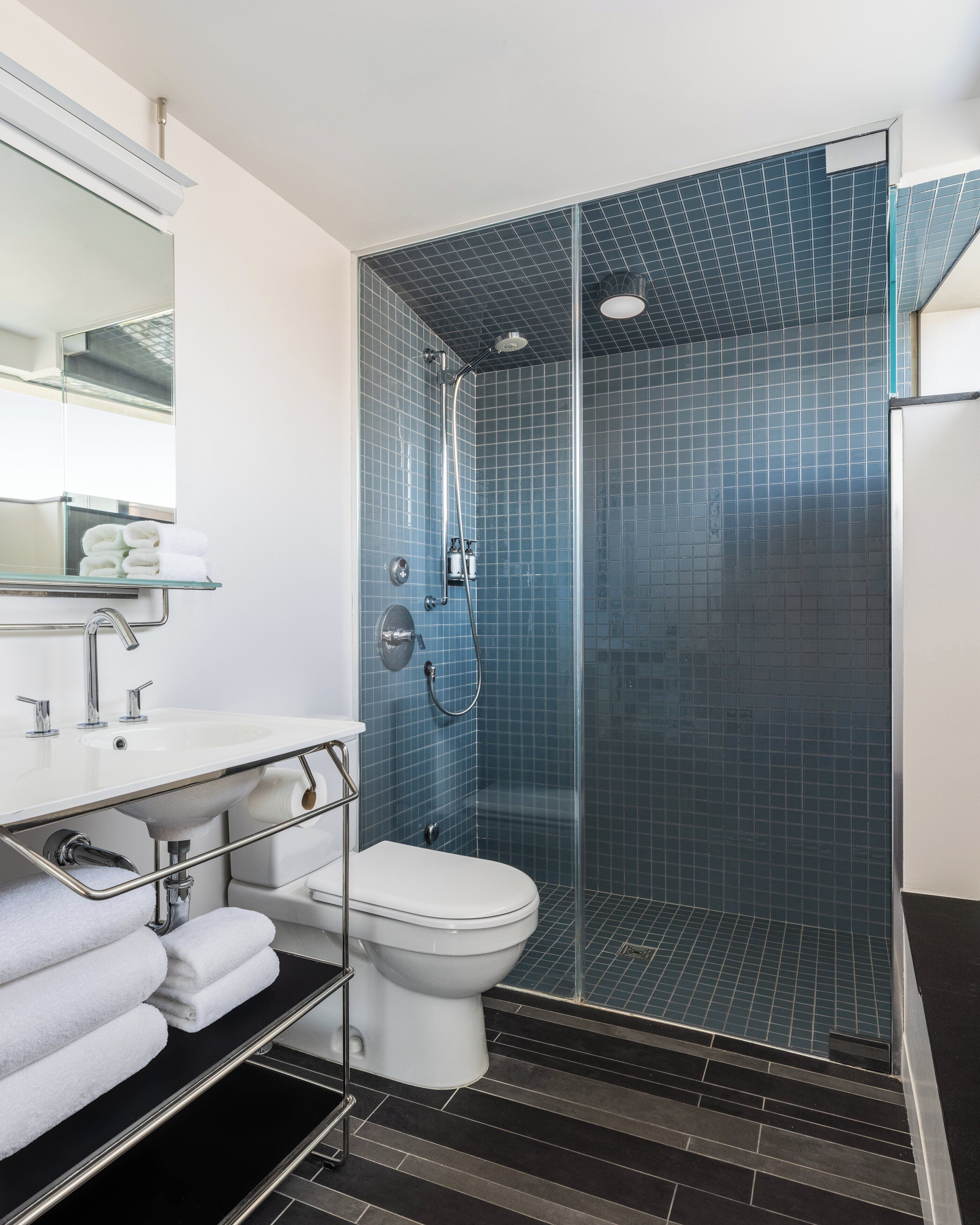 Un baño moderno con ducha acristalada, inodoro blanco y lavamanos con toallero.