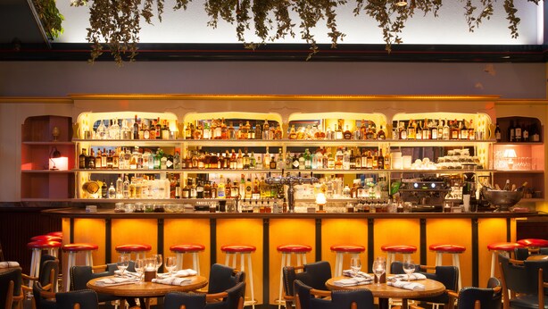 A bar area with multiple stools and tables, shelves stocked with bottles, and a bar counter with various items. - The Standard East Village (New York)