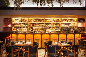 Una zona de bar con varios taburetes y mesas, estantes llenos de botellas y una barra con diferentes objetos.