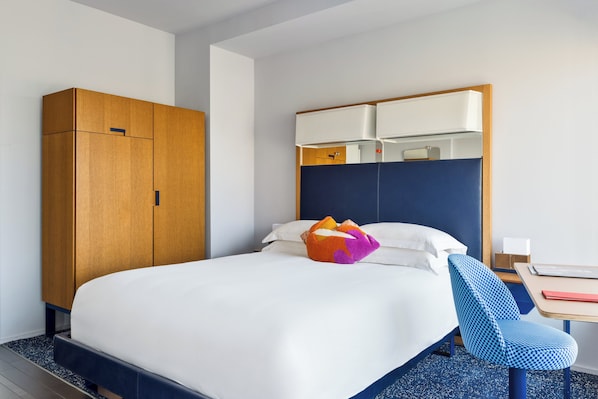 Habitación de hotel con cama, armario de madera, silla azul y escritorio con lámpara.