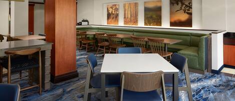 Un comedor de hotel con un banco tapizado en verde, mesas y sillas de madera.