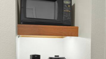 A kitchen area with a microwave on a shelf, a coffee maker, and a trash bin.