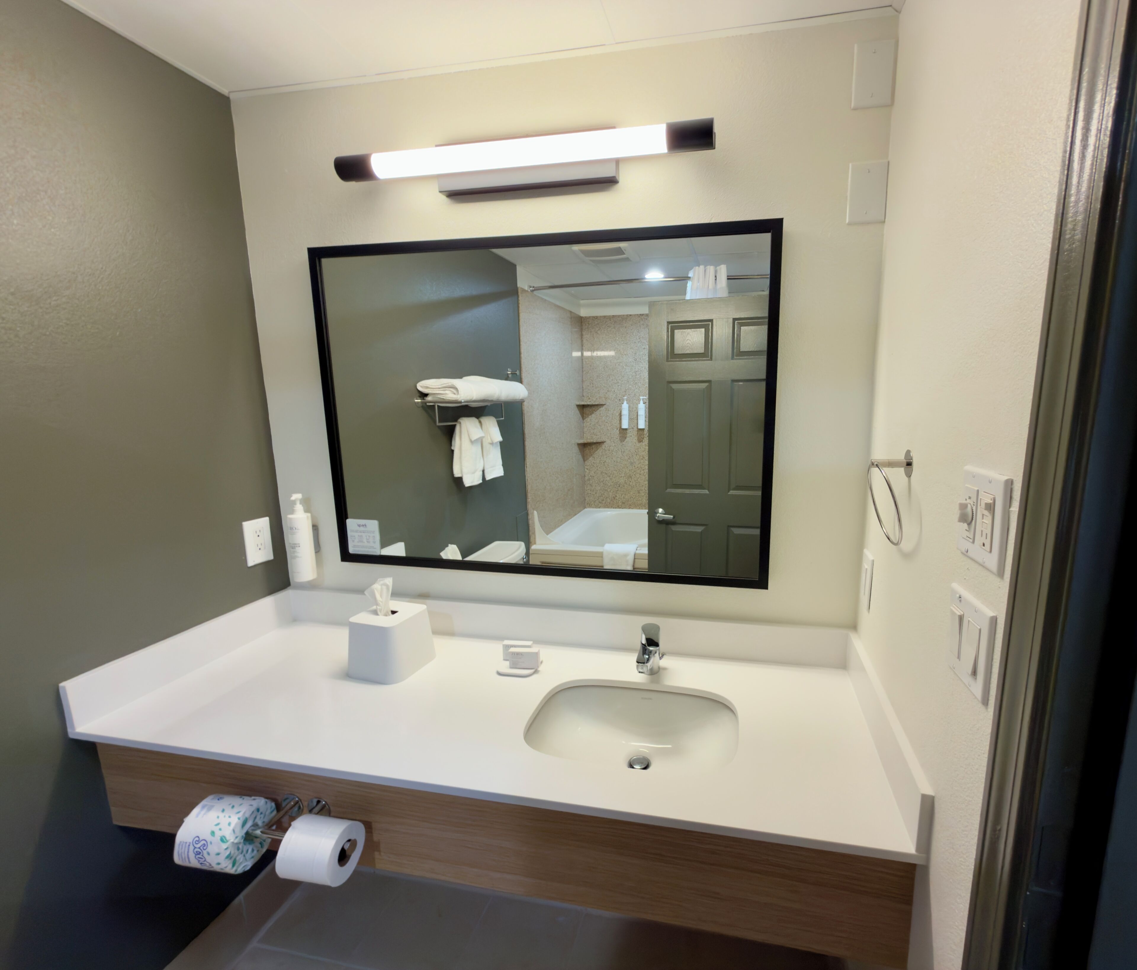 A modern bathroom with a large mirror, a sink, and a toilet paper holder.