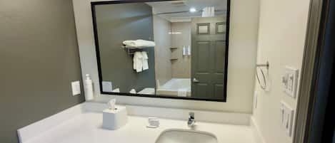 A modern bathroom with a large mirror, a sink, and a toilet paper holder.