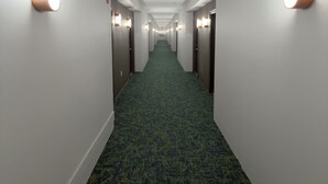 A hotel hallway with carpeted floors, white walls, and wall-mounted light fixtures. - Spark by Hilton Galloway Atlantic City (Absecon)