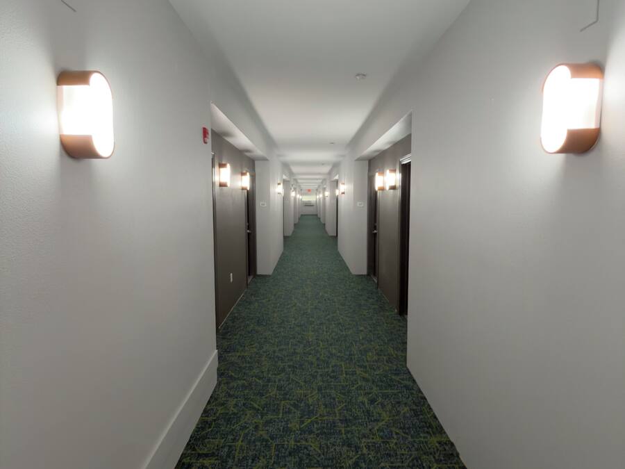 Un corridoio d'hotel con pavimenti in moquette, pareti bianche e luci a parete.