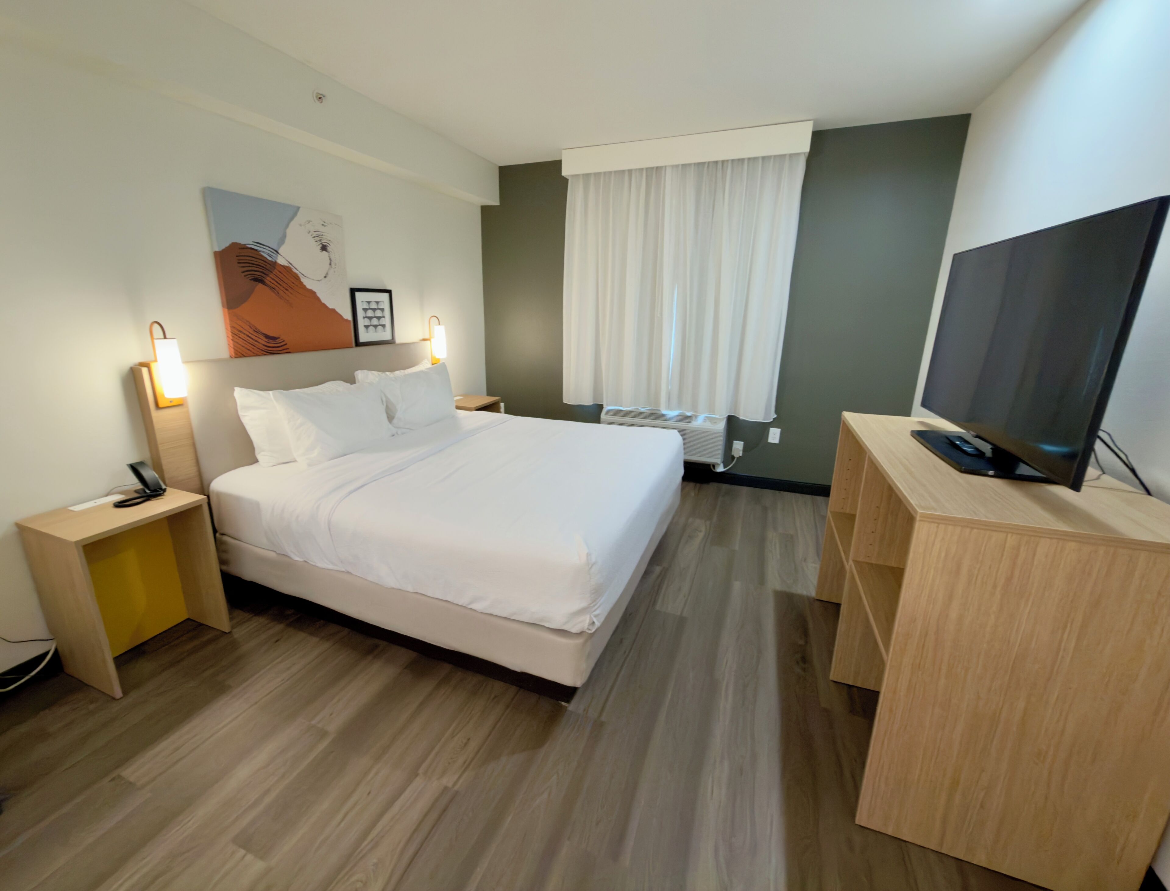 A hotel room with a bed, bedside tables, a TV, and a window with curtains.