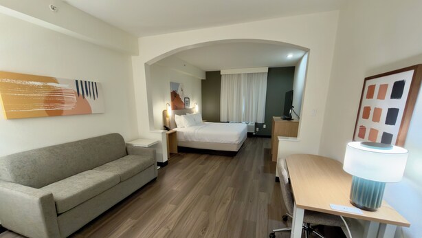 A hotel room with a sofa, a bed, a desk with a lamp, and a painting on the wall. - Spark by Hilton Galloway Atlantic City (Absecon)