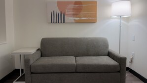 A grey sofa, a small white side table, a floor lamp, and a wall with a piece of abstract art. - Spark by Hilton Galloway Atlantic City (Absecon)