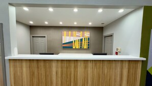 A reception desk with a wooden panel backdrop, a colorful abstract painting, and a ceiling with recessed lighting. - Spark by Hilton Galloway Atlantic City (Absecon)