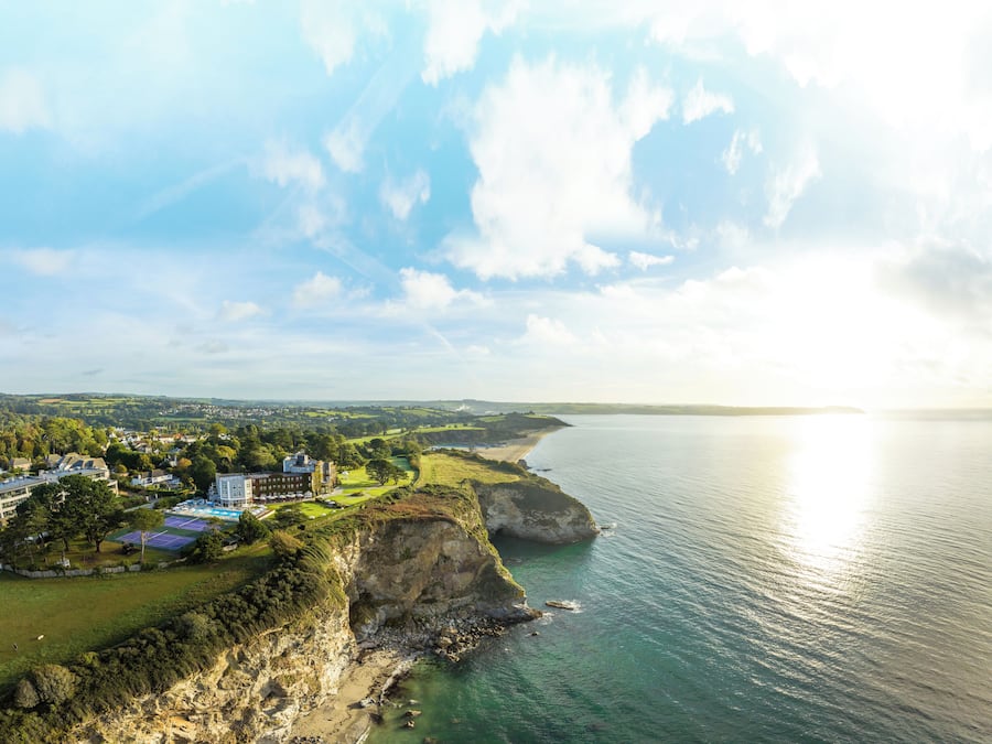 A coastal property with a tennis court, beach, and cliff overlooking the sea.