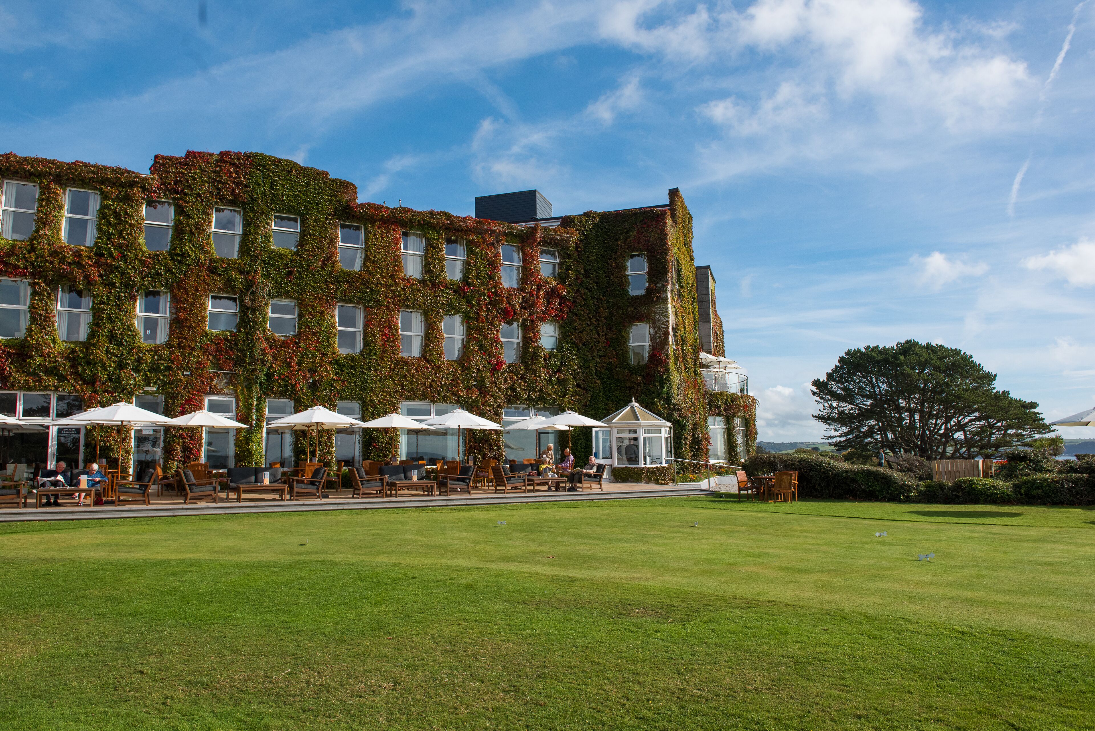 A building with ivy-covered exterior walls, outdoor seating with umbrellas, and a well-maintained lawn.