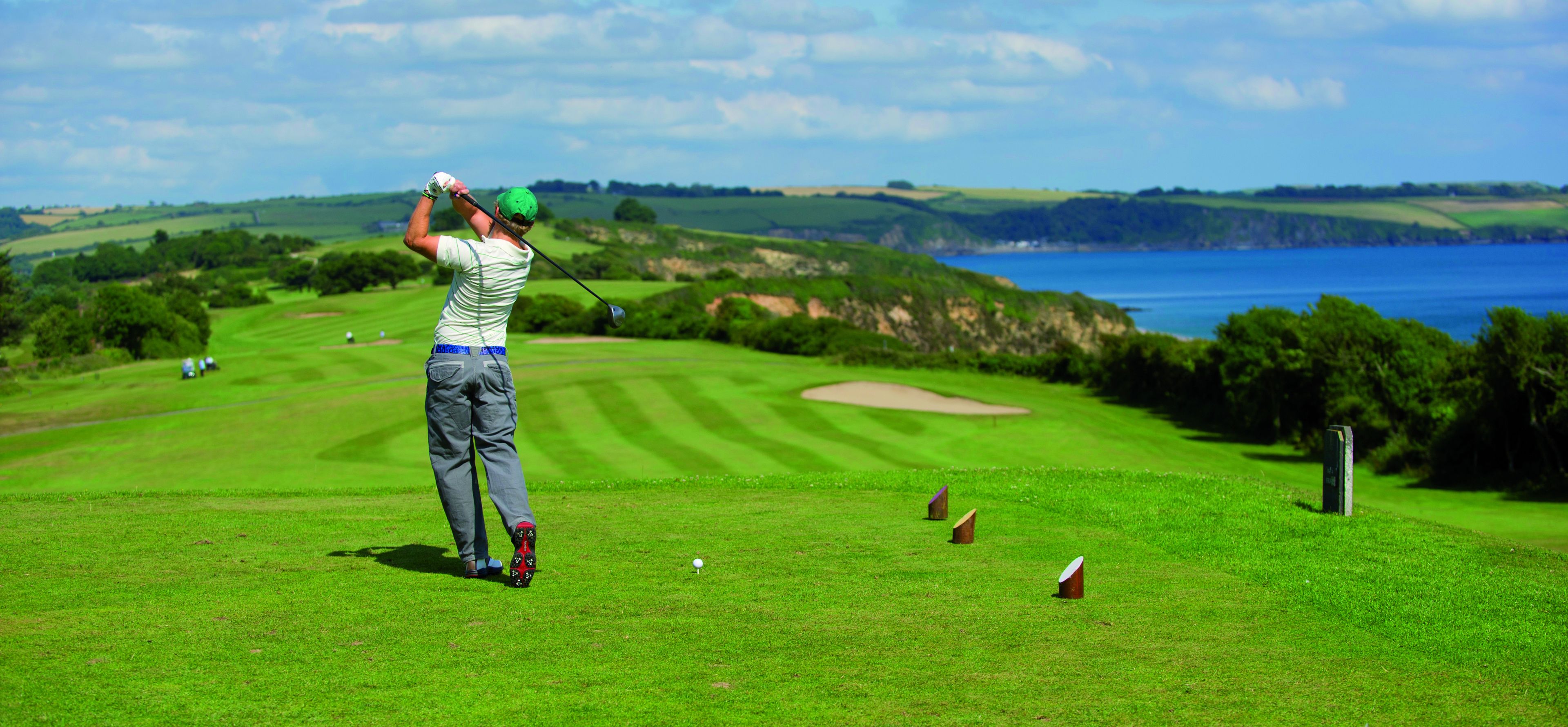 A golfer on a golf course with a scenic view of the sea and hills in the background.