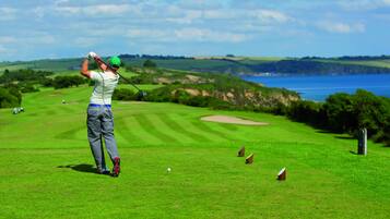 A golfer on a golf course with a scenic view of the sea and hills in the background.
