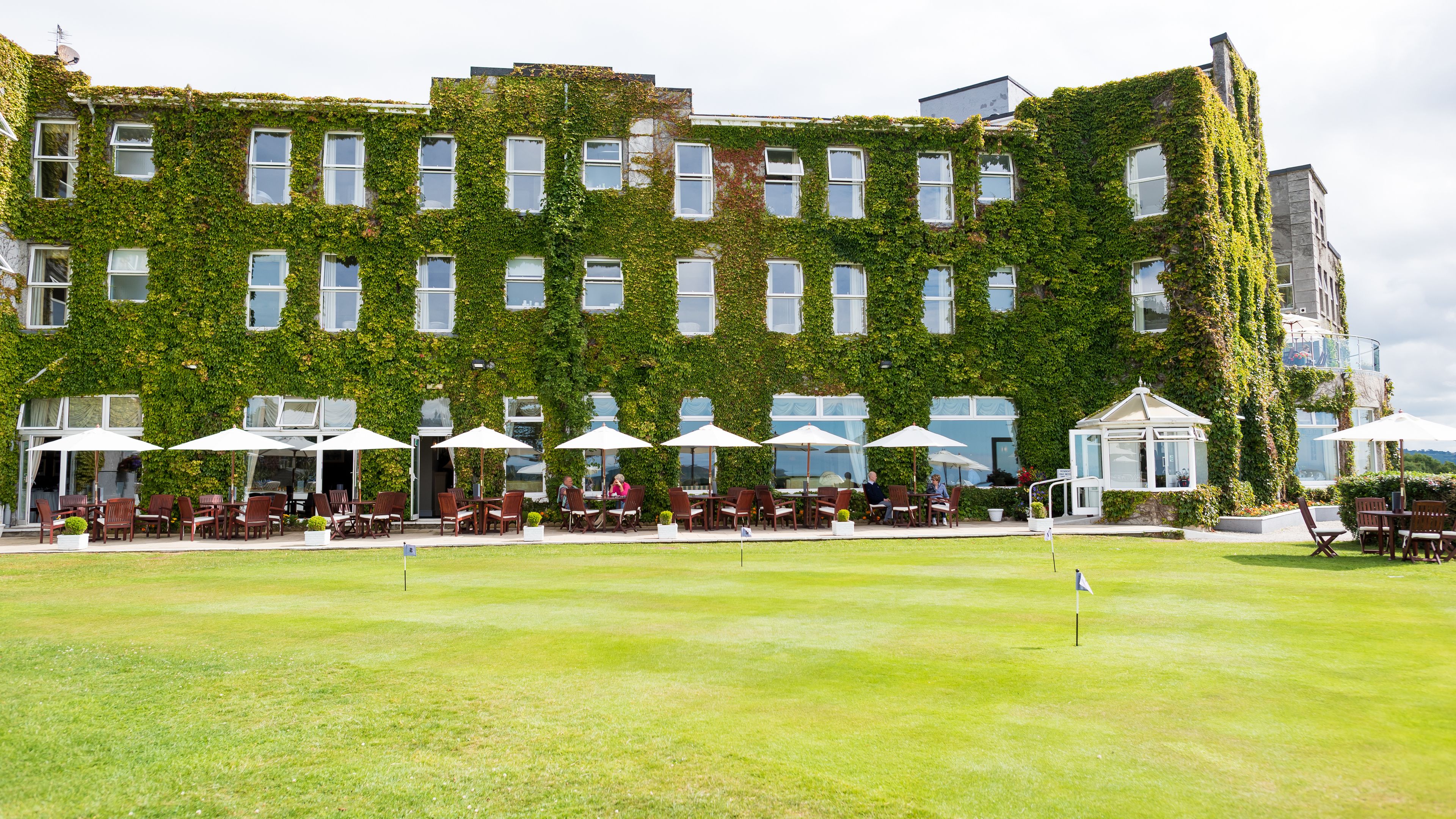 A building with a green ivy-covered exterior, outdoor seating with umbrellas, and a well-maintained lawn.