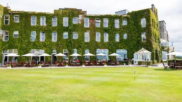 A building with a green ivy-covered exterior, outdoor seating with umbrellas, and a well-maintained lawn.