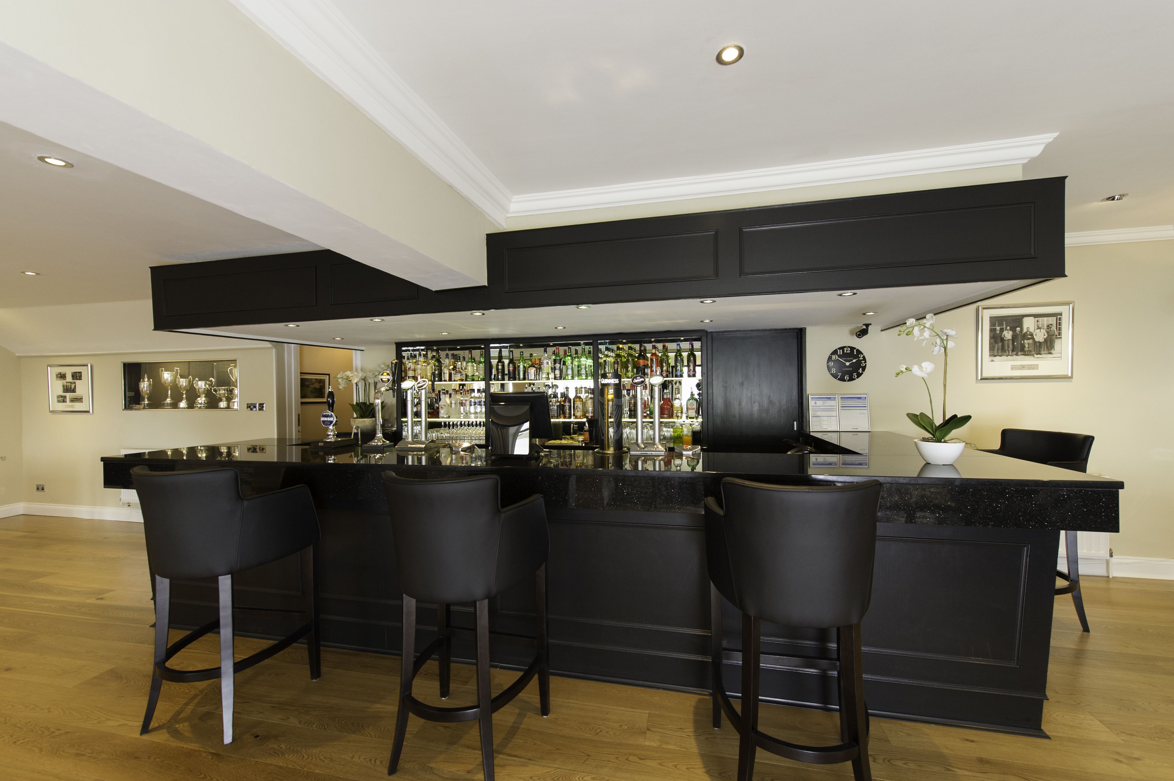 Zona de bar con mostrador negro, taburetes y una variedad de botellas y vasos.