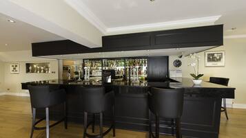 Zona de bar con mostrador negro, taburetes y una variedad de botellas y vasos.