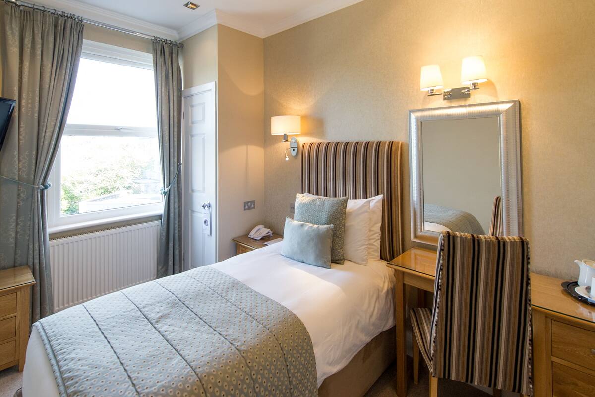 A hotel room with a bed, bedside table, lamp, mirror, and a TV mounted on the wall.