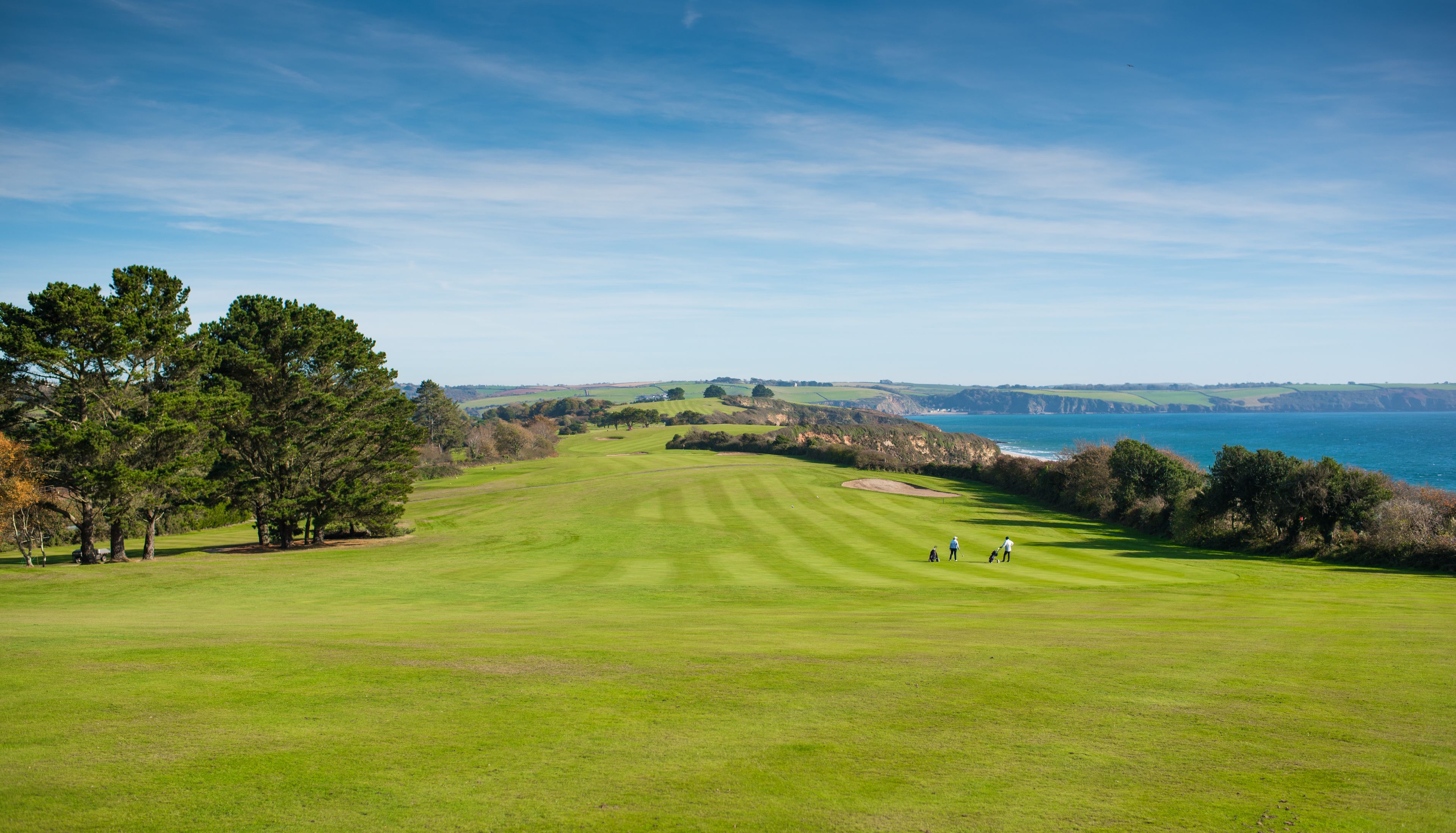 Campo de golf con vista al mar, que incluye una masa de agua y acantilados a la distancia.