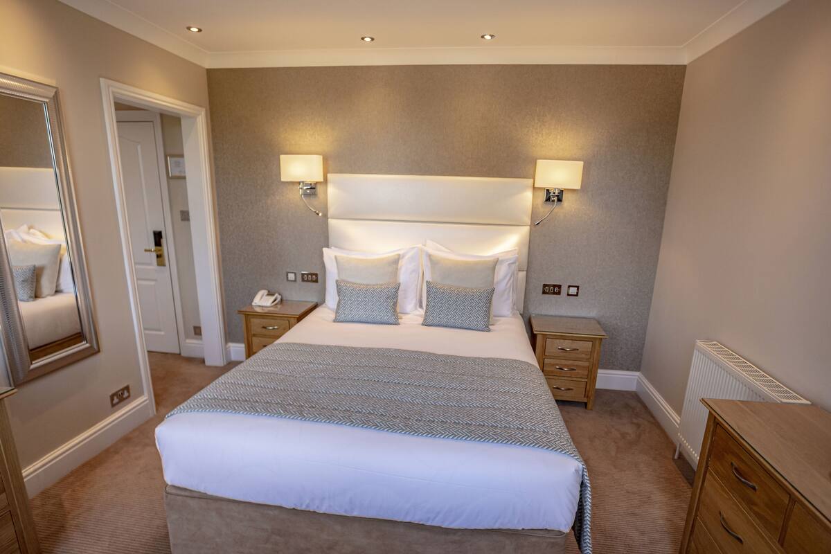A hotel room with a large bed, bedside tables, a mirror, and wall-mounted lamps.