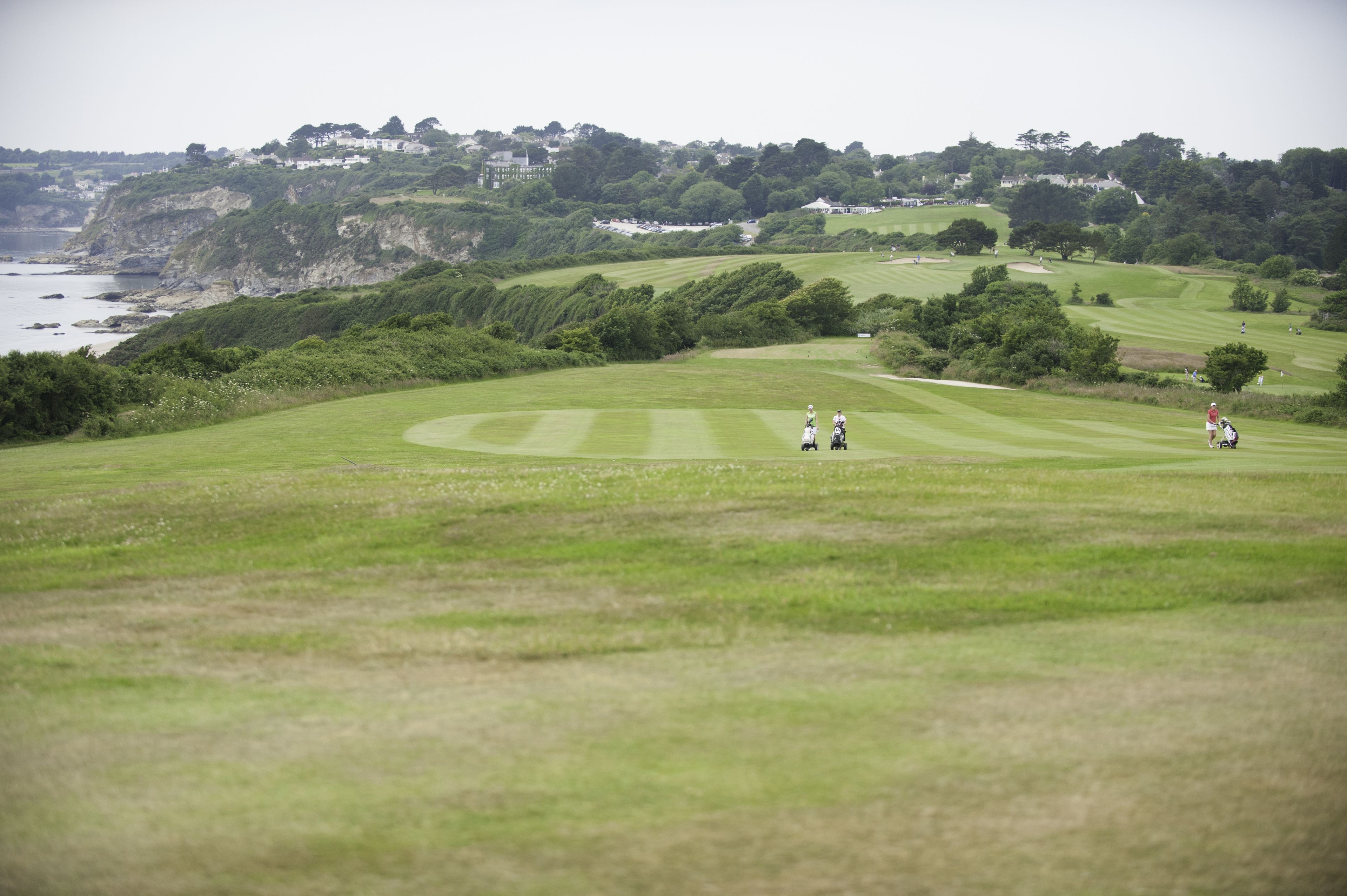 A golf course with a coastal backdrop, featuring rolling hills and a view of the sea.